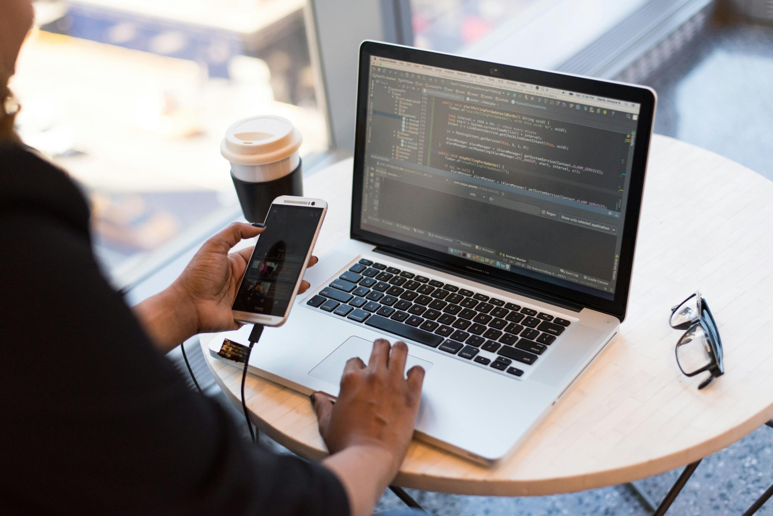 pexels-photo-1181244-1181244 Developer working remotely, coding on a laptop with phone in hand, showcasing modern work culture.